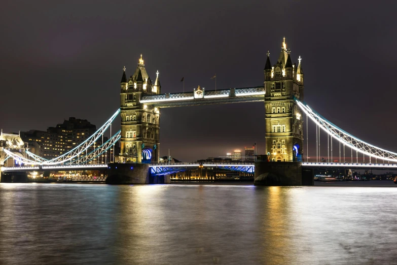 there is a tower bridge with lights on over the water