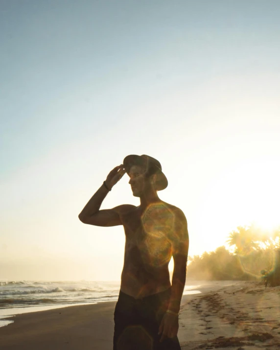 the man is looking down on his hat while standing at the beach