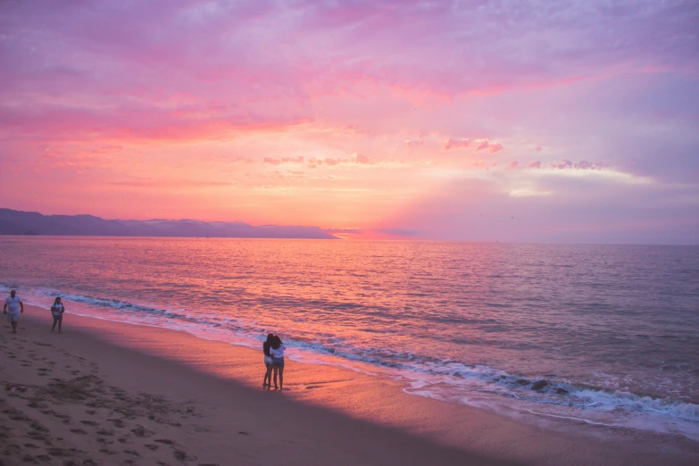 some people at the beach while the sun sets