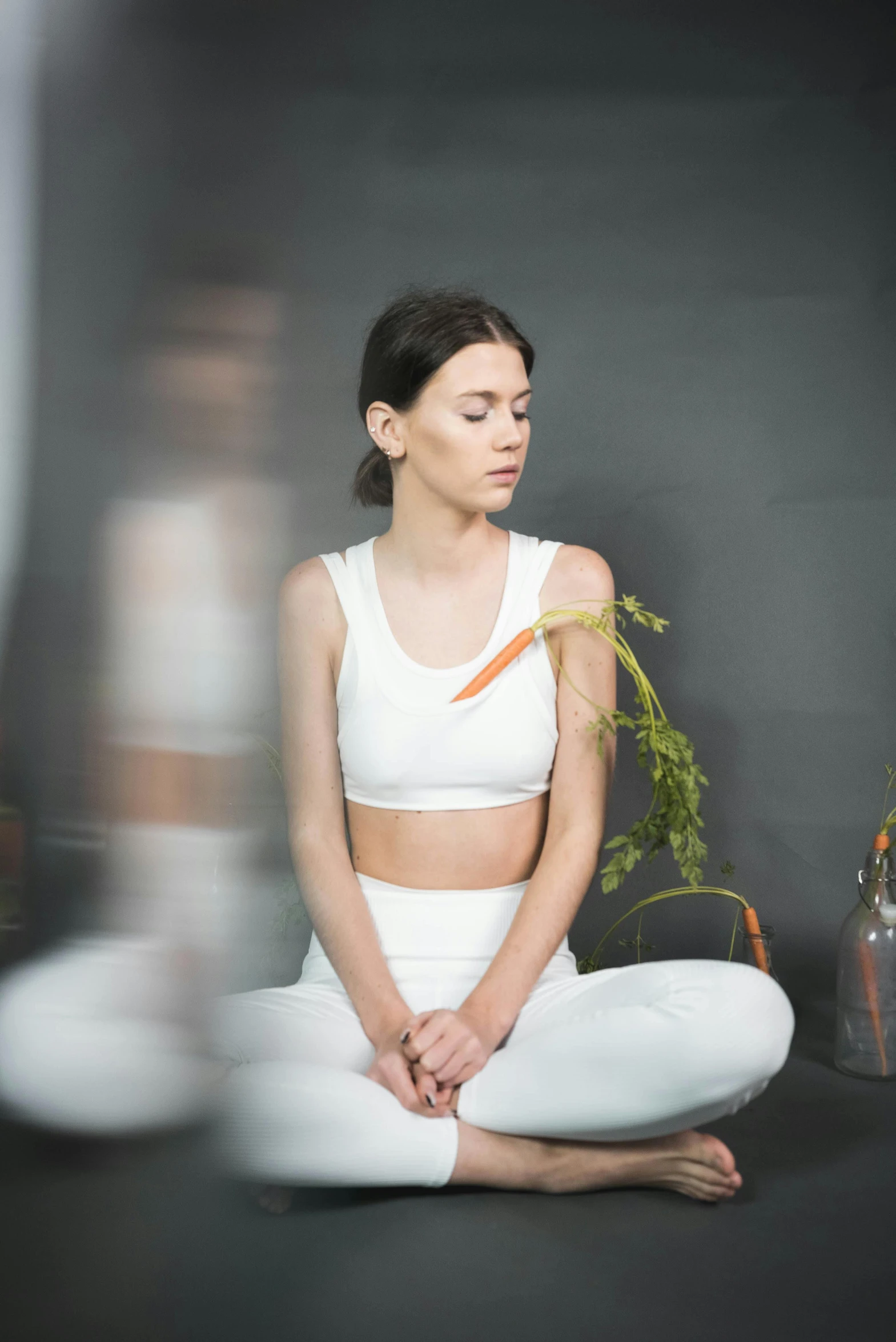 a woman in white sits in a yoga position and holds an orange flower