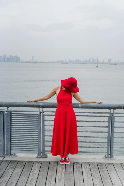 a woman in a red dress stands at the edge of a dock