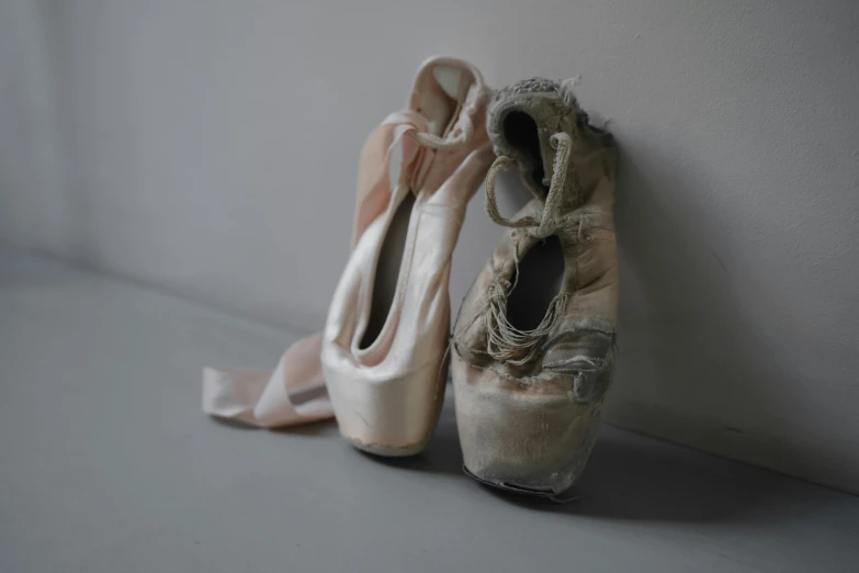 two dirty, worn up ballet shoes leaning against a wall