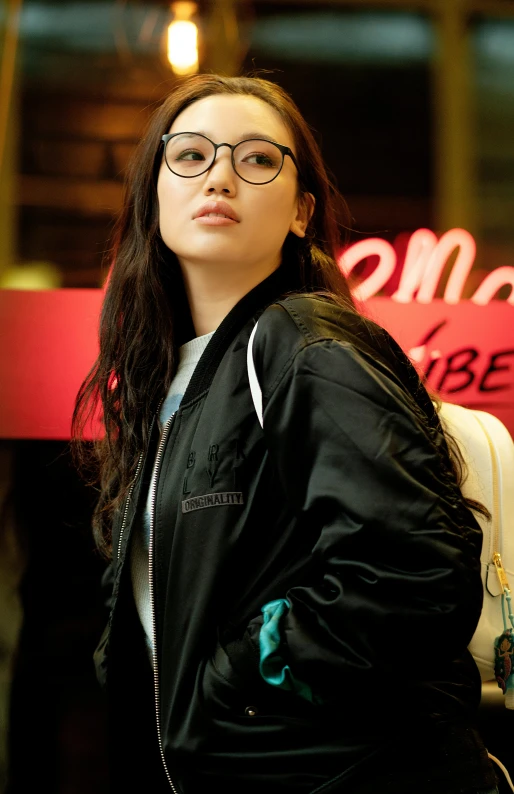 a girl wearing glasses stands in front of a neon sign