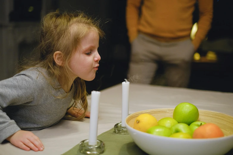 little girl looking at a bowl of fruit with candles