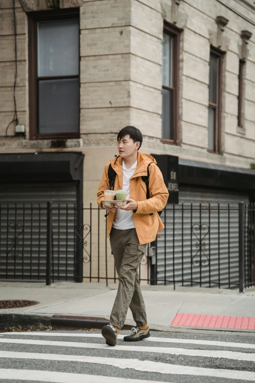 man in orange jacket and khaki pants walking with cup