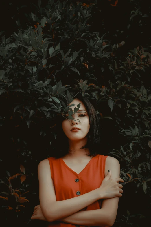 a woman in an orange top posing in front of a bush