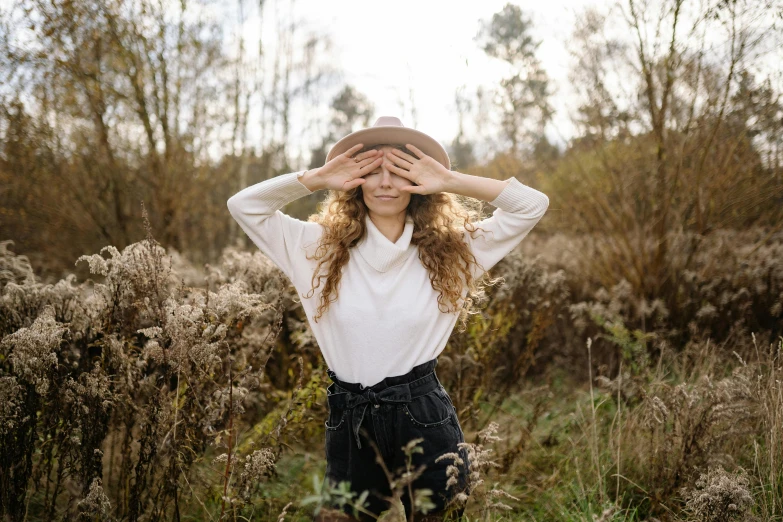 the girl covers her face with her hands while standing in a field