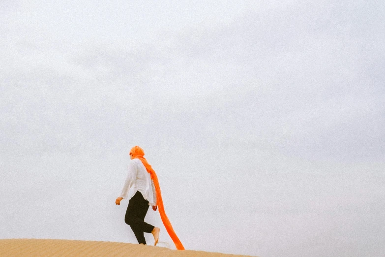 a man walking across a beach next to a large orange kite
