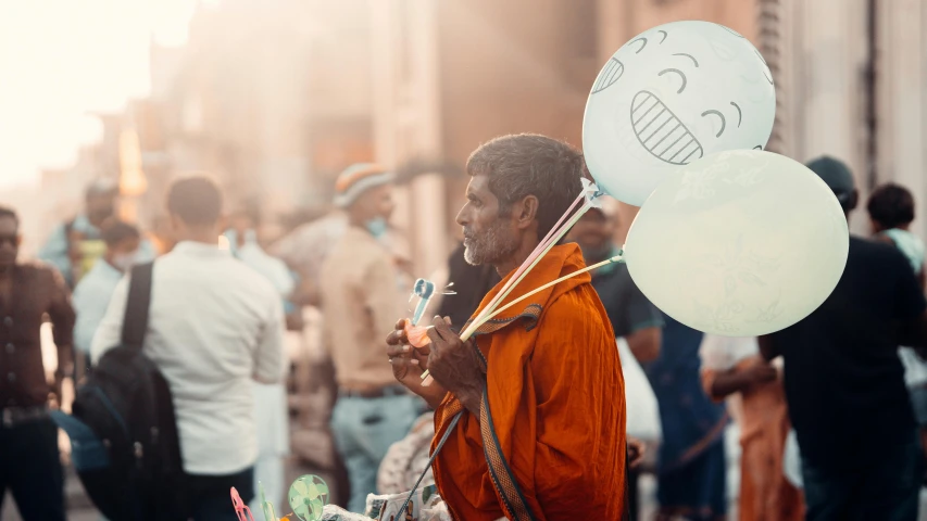 man holding up three balloons in the street