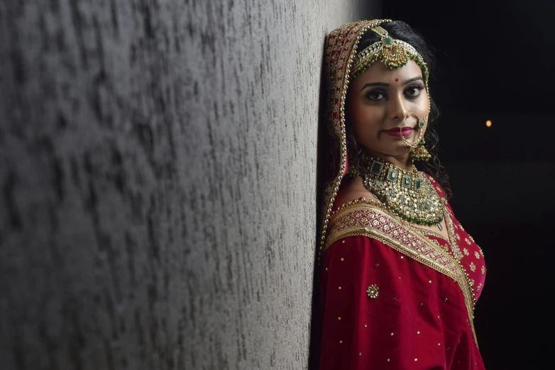 a woman dressed in a red bridal gown leans against a wall