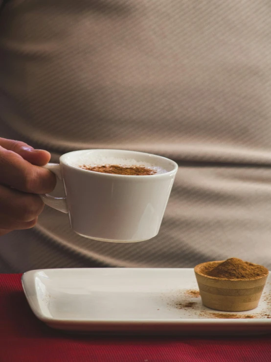 someone holding a cup and saucer over a white plate