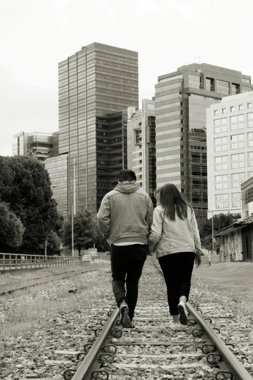 two people walking down train tracks near tall buildings