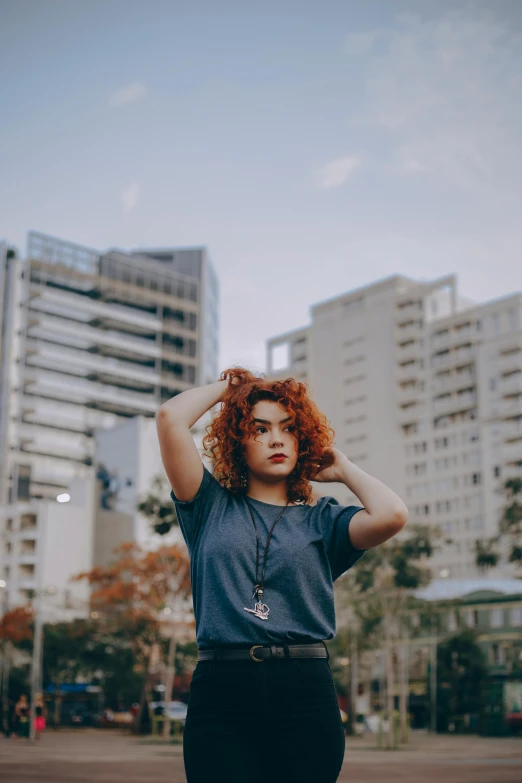 red - headed woman with curly hair and blue shirt in a city park