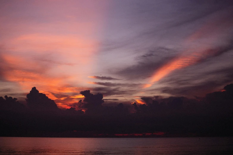 sunset at the edge of a lake with many clouds in the background