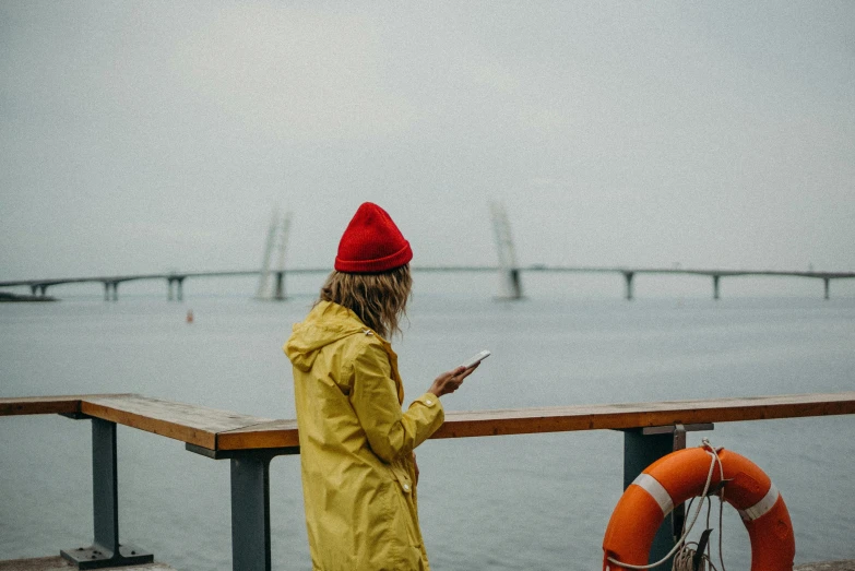 a girl on her phone looks down at the ocean