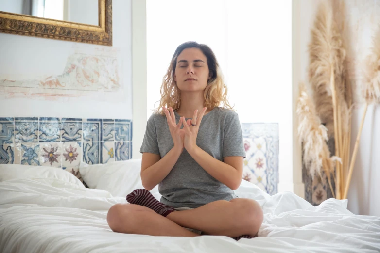 a woman sitting on top of a bed in a gray shirt doing yoga