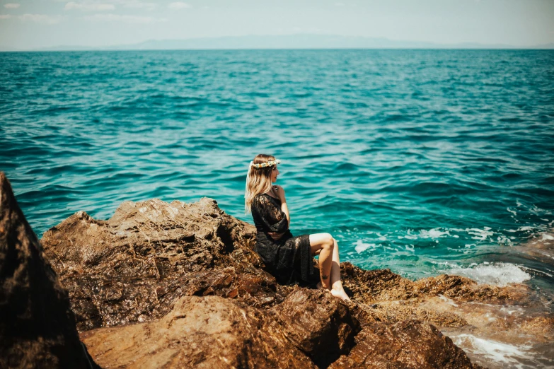 a woman sitting on a rock by the ocean