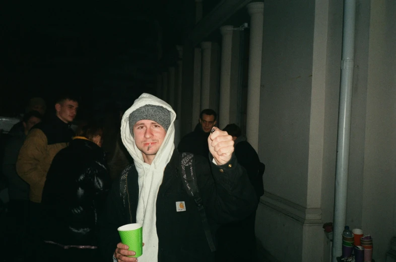 a person wearing a hoodie drinking out of a green cup