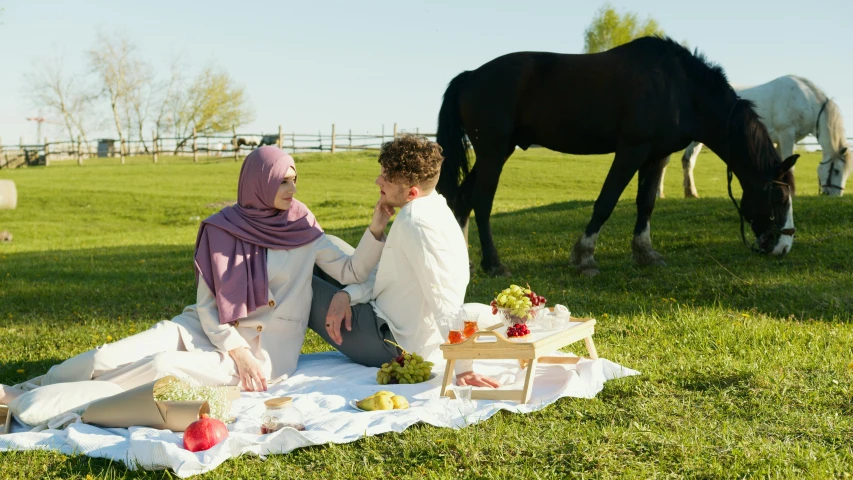 a young couple is sitting on a blanket and picnics next to horses