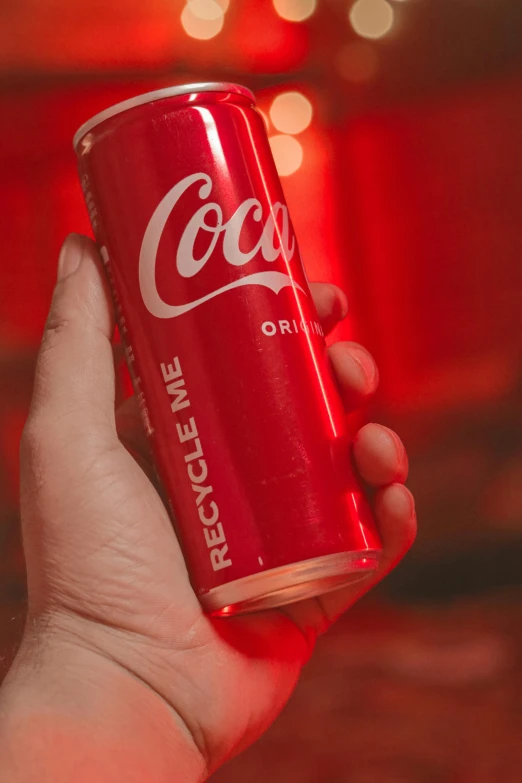 a hand holding up a soda can with red light from the ceiling