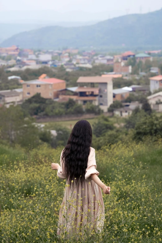 there is a woman standing in the grass looking at the city