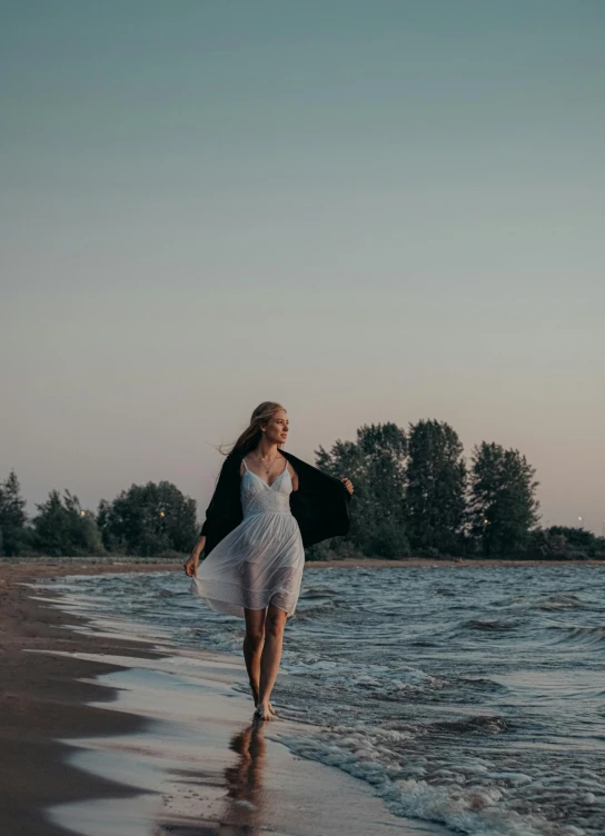 a woman walking on the beach with her dress blowing in the wind