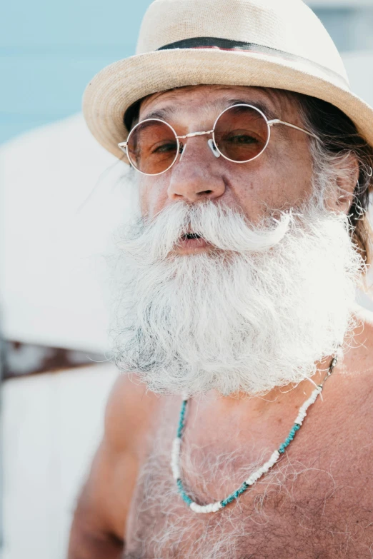 a man wearing glasses, a hat and beads looks into the distance