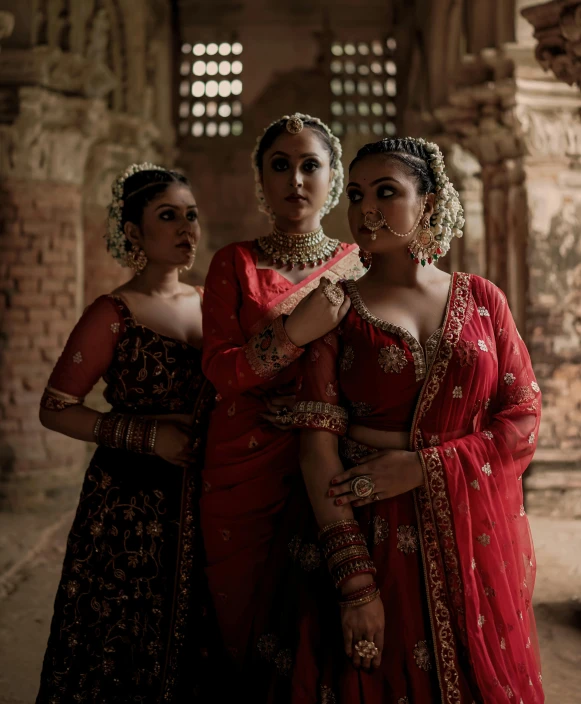 three women in red and gold sari pose for a pograph