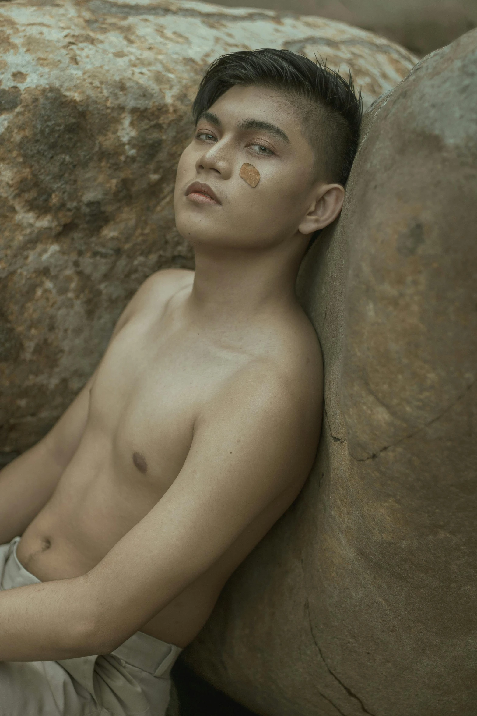 a shirtless man leaning against the rock