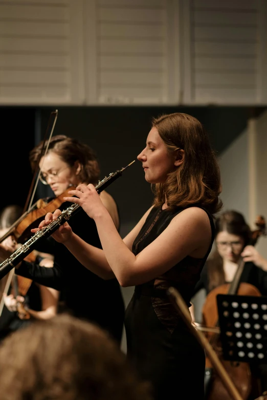 a woman playing flute in orchestra with other people looking on