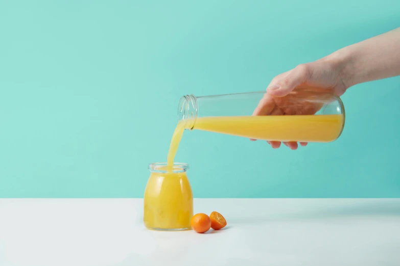 a hand is pouring orange juice into a clear glass