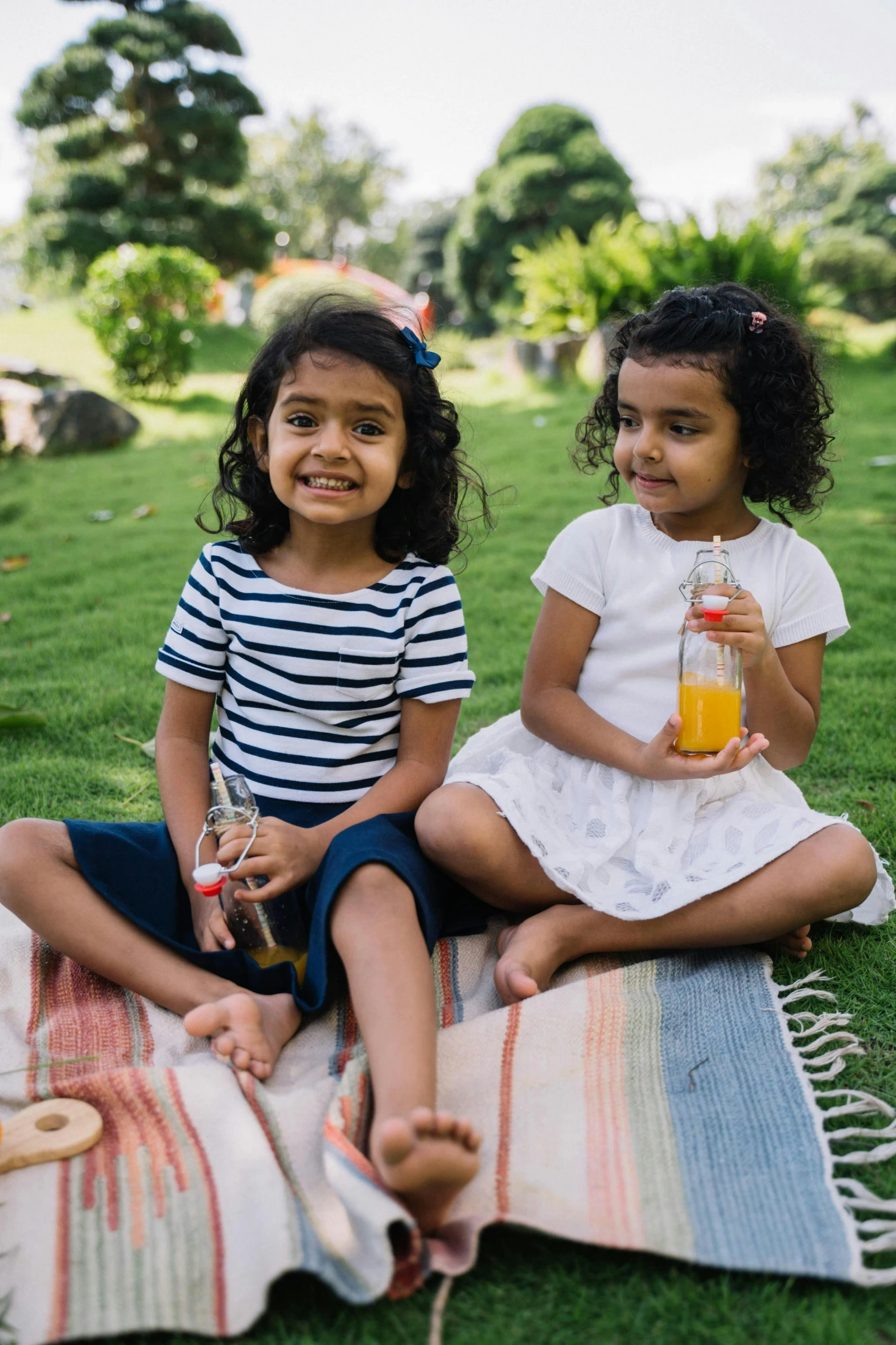 two little girls holding small beverages sitting on a blanket