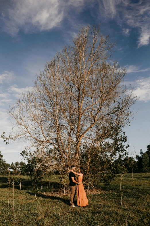 two people standing next to a tree in the grass