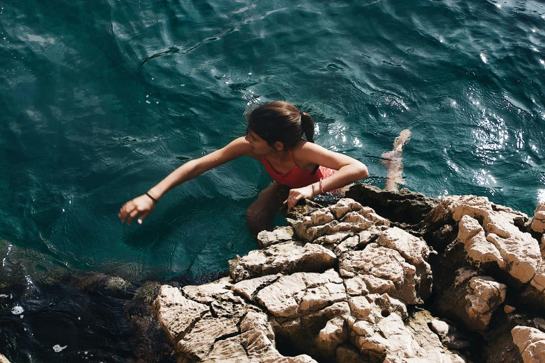 a girl in a red swimsuit floating from rocks into the water