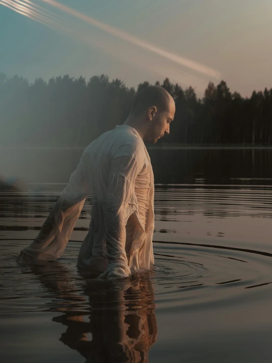 a man in white shirt sitting on the edge of a river in water