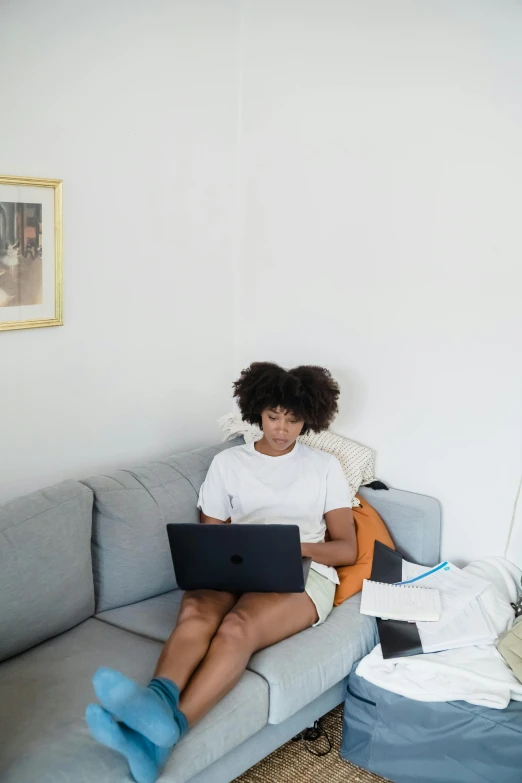 an african american woman is sitting on a couch working on her computer