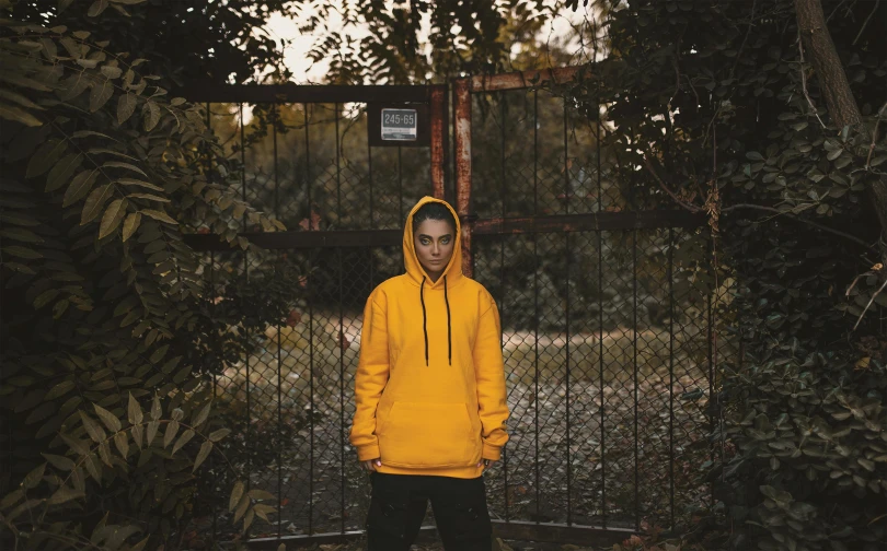 a young man wearing a yellow hooded jacket standing in front of an iron fence