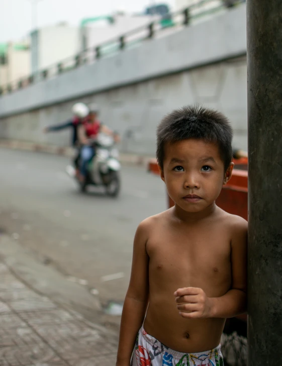 a little boy standing next to a pole by the road