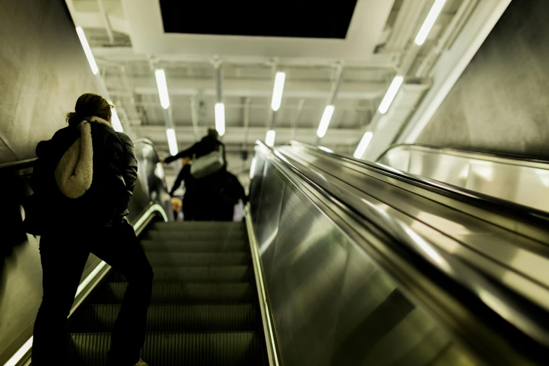 man carrying luggage on an escalator with people walking down the stairs in background