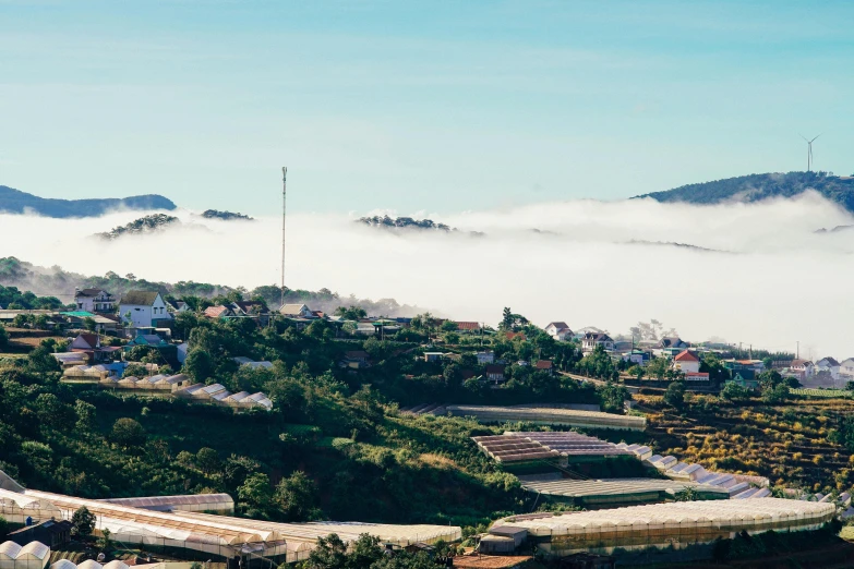 a lush green hillside with houses and fog in the air