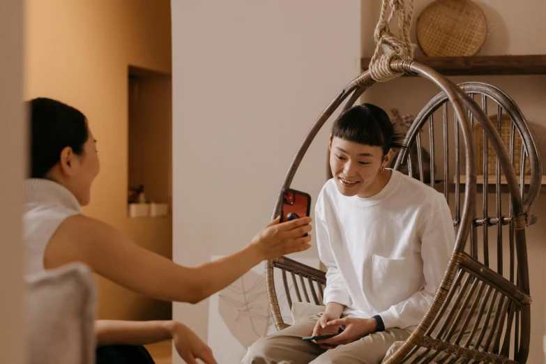 a young asian woman sits on a chair and looks at her phone