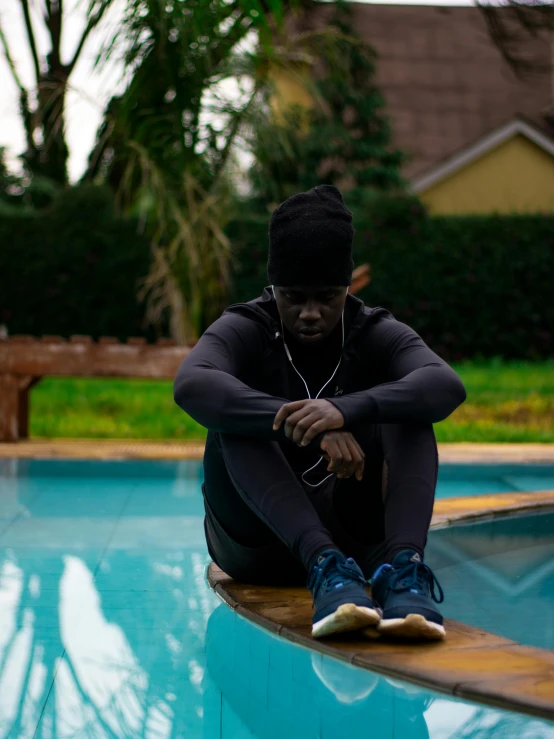 a young person sitting on the edge of a swimming pool listening to earbuds