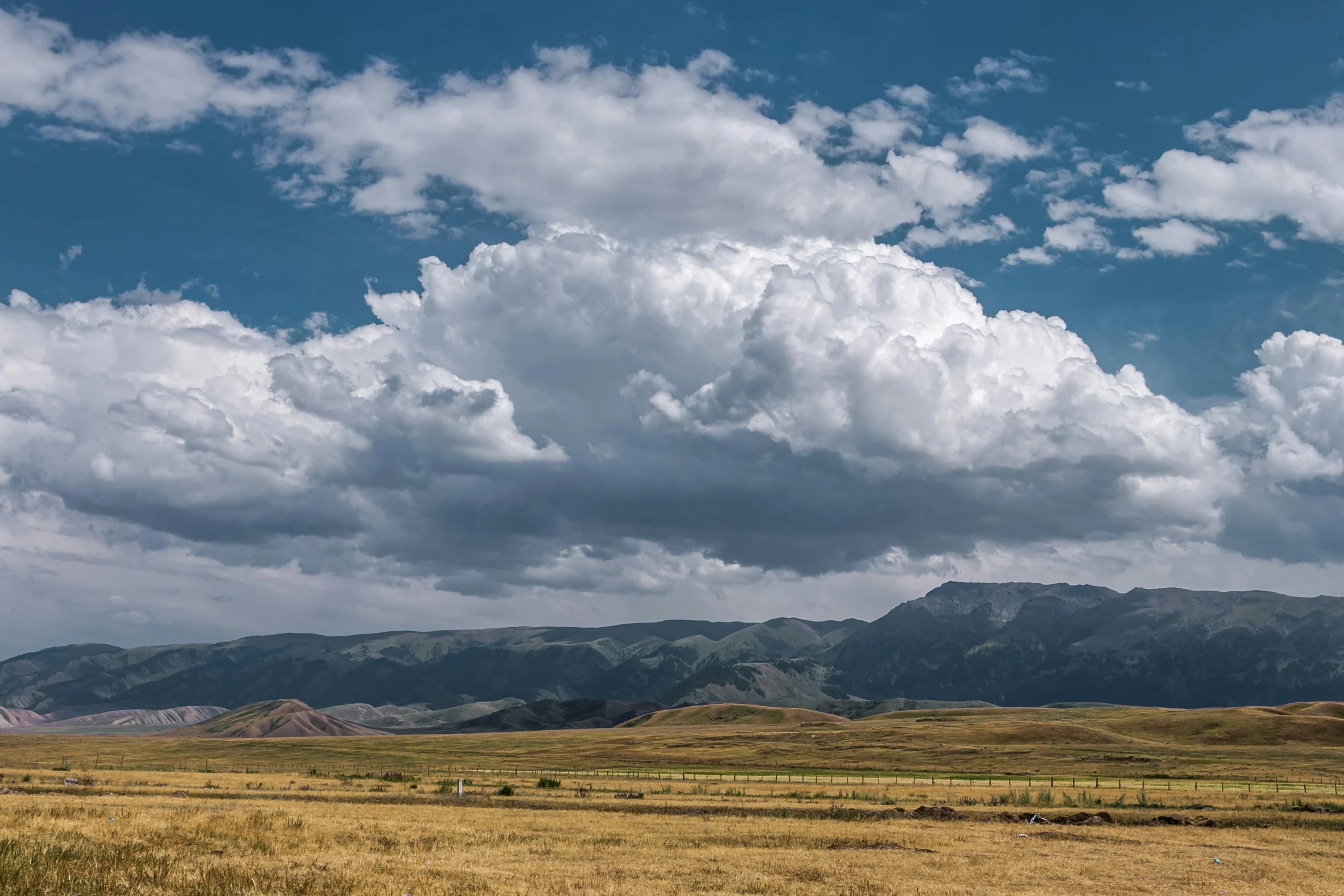 the sky above mountains is very cloudy and some grass