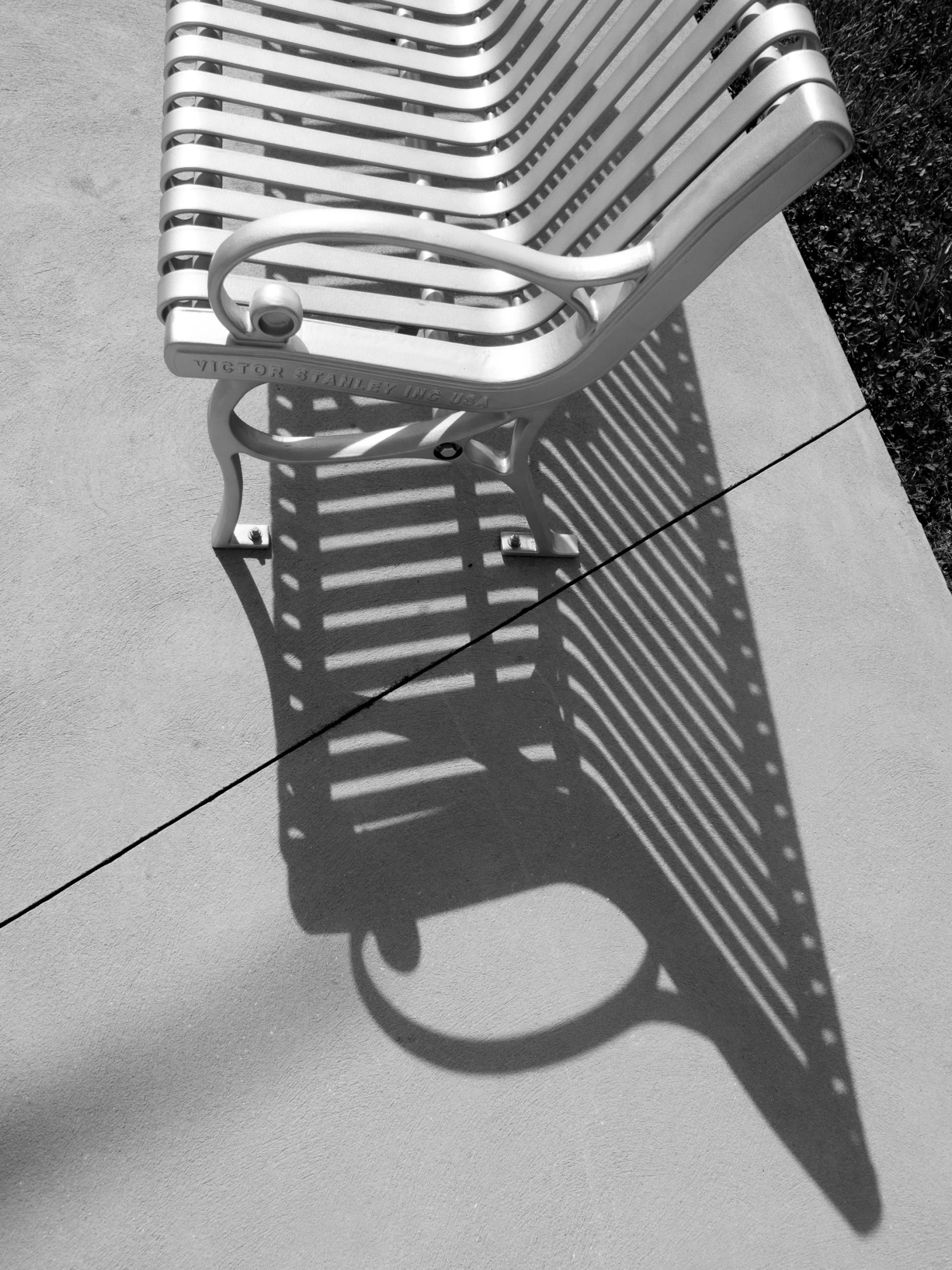 a long bench casts the shadow of a slatted metal chair