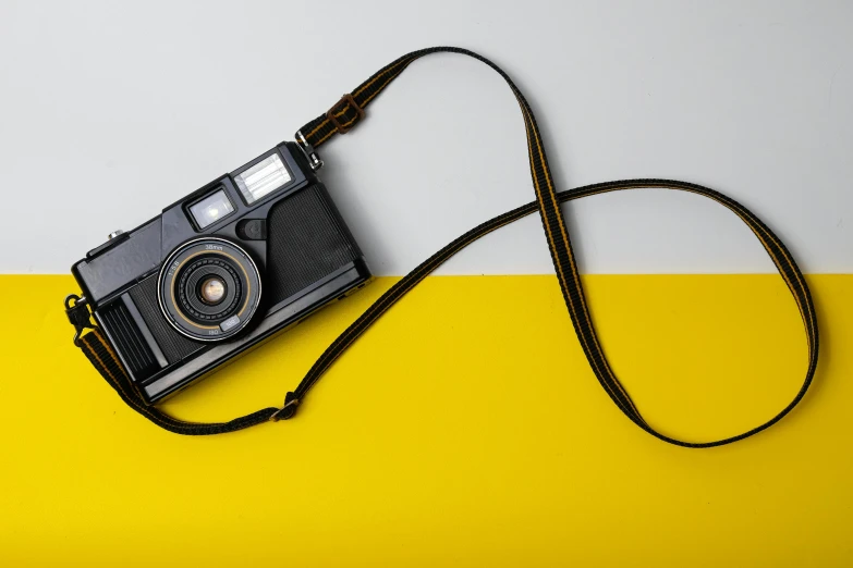 the camera has a strap and is laying on top of the yellow and white surface