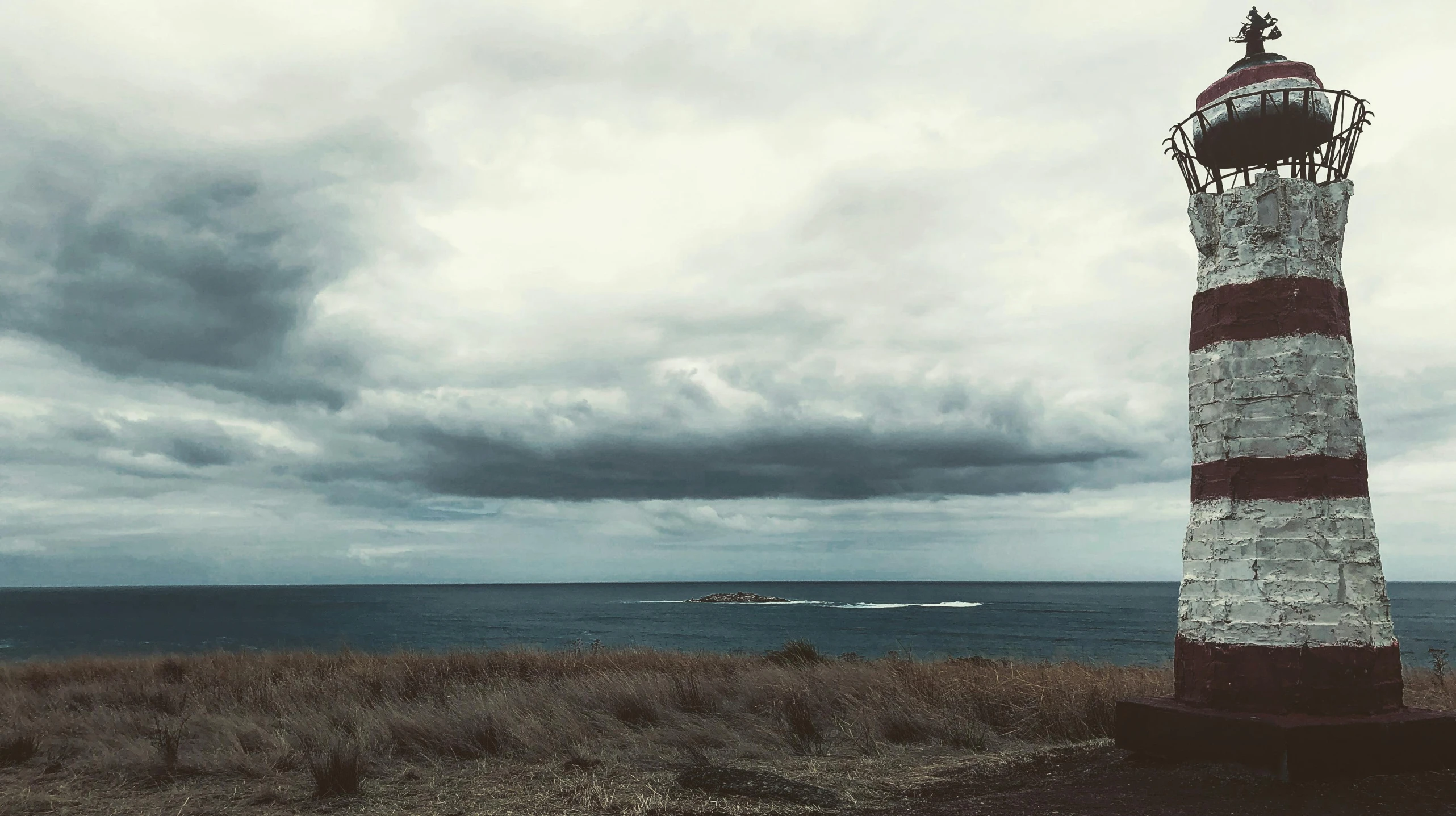 an old looking lighthouse at the edge of a sea with stormy clouds