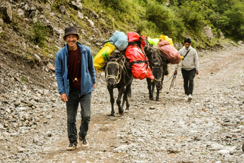 two men walking down a rocky road with horses