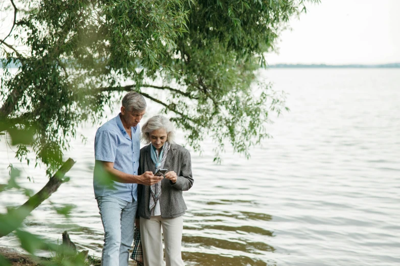 an elderly man and woman standing next to the water