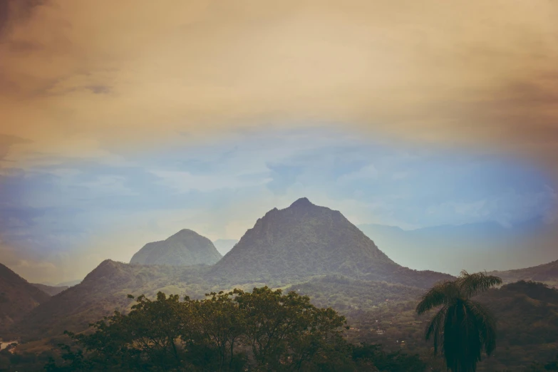 some trees and mountains under a cloudy sky