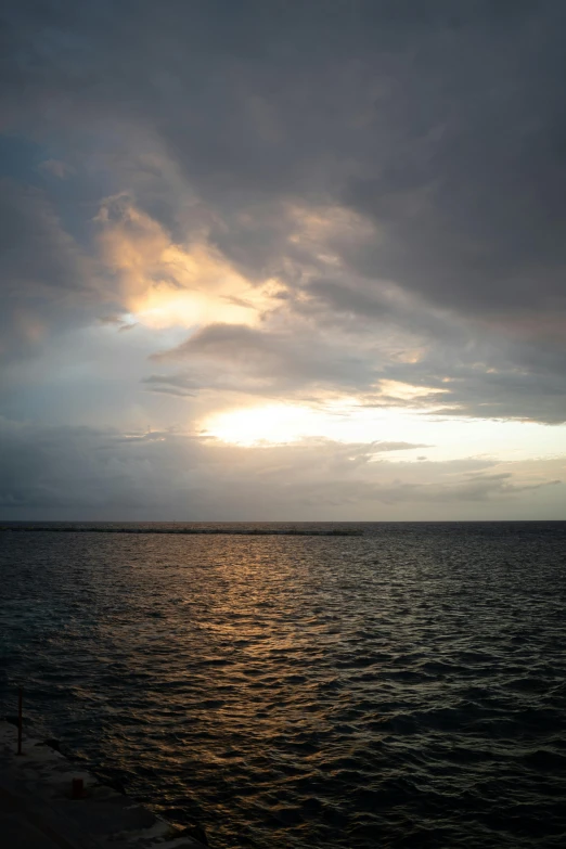 the sun is setting over the ocean with dark clouds